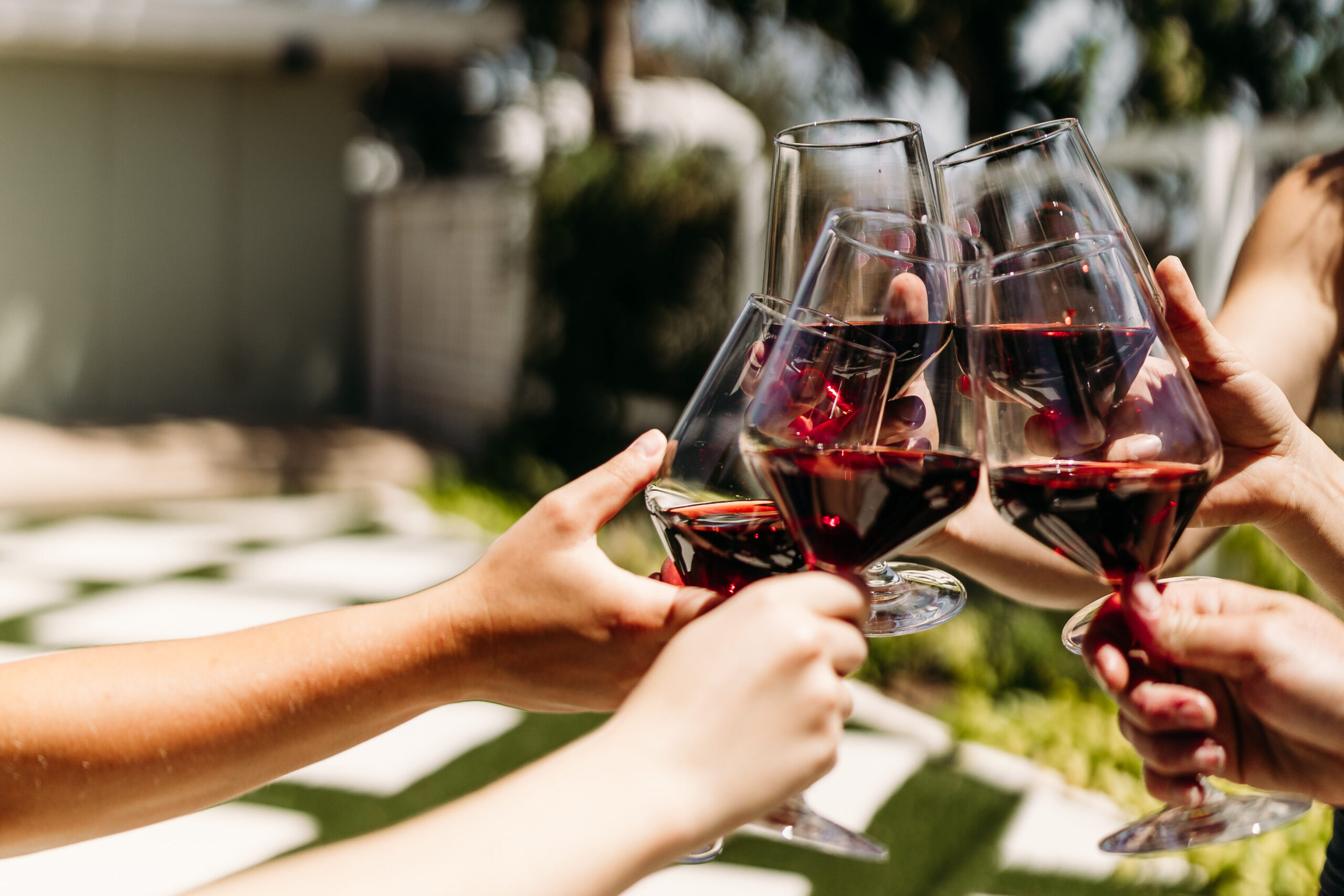 Rehearsal dinner venue Austin Wedding venue Texas Hill Country, Dripping Springs. Four guests toasting with red wine on the antique rose veranda at Rose Haven Event Venue. Bridal shower. Bride. Groom.